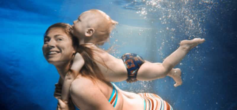 Mother swimming with baby boy(12-15 months) on back, underwater view