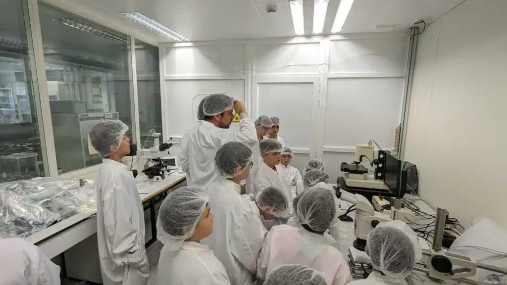 Cursos de robótica y programación para niños en Valencia 5 Grupo de niños con bata y gorro trabajando con microscopios en un aula de ciencia