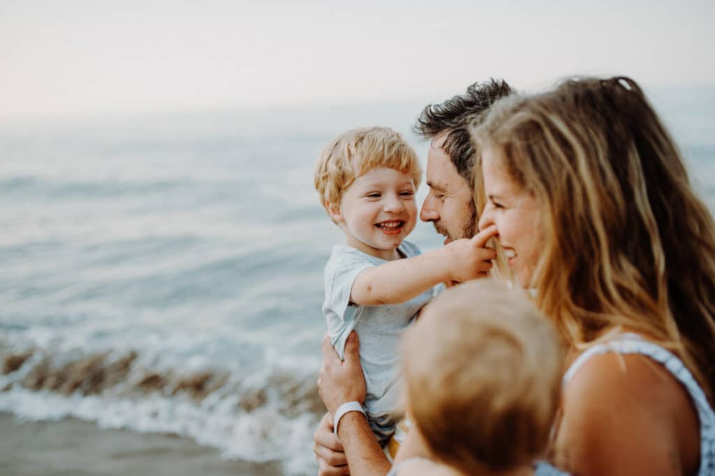 Viaja en familia con Buscounchollo 1 A young family with two toddler children standing on beach on summer holiday.