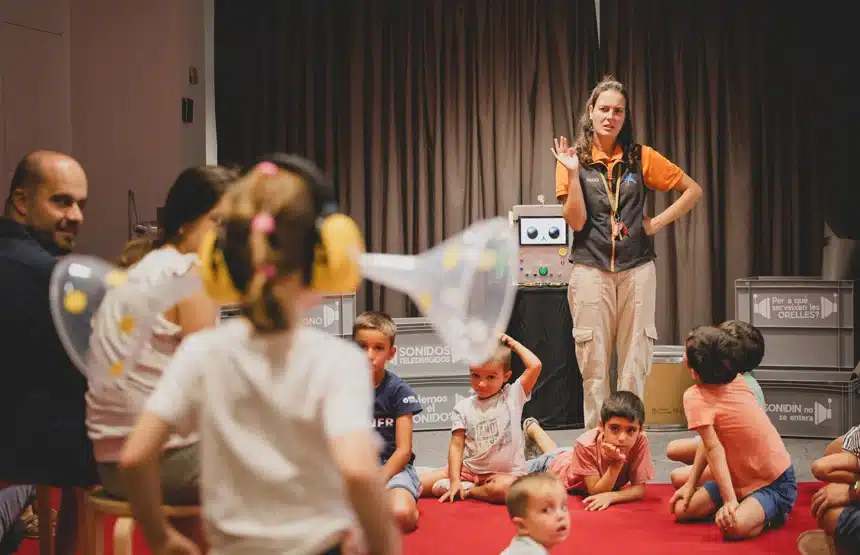 Exposiciones para niños y familias en CaixaForum València, con visitas-taller 5 Niños sentados en el suelo y una niña con cascos de protección y un embudo en el taller Sonidos teledirigidos de CaixaForum València