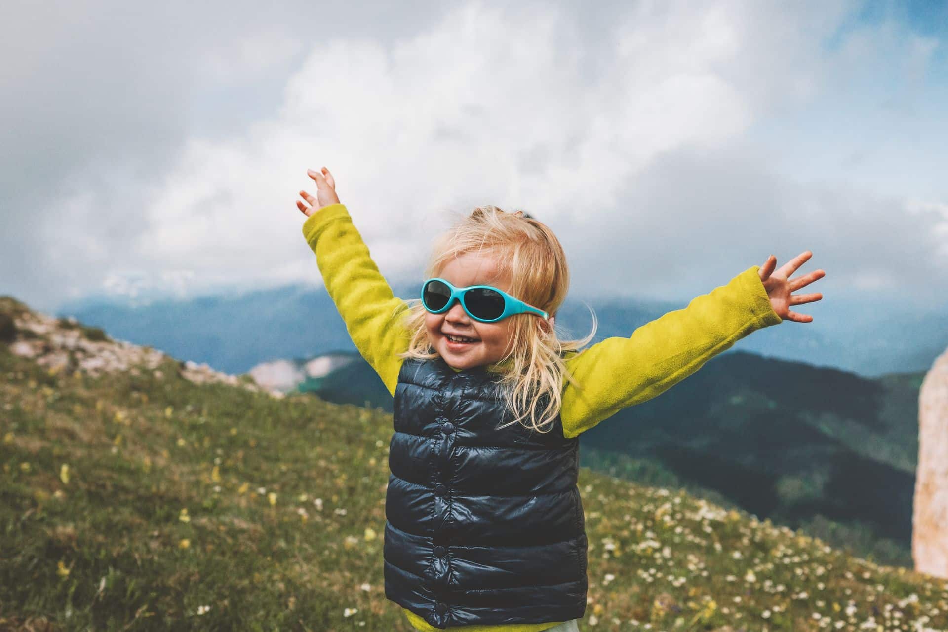 Niña con gafas de sol y los brazos abiertos en un prado de montaña