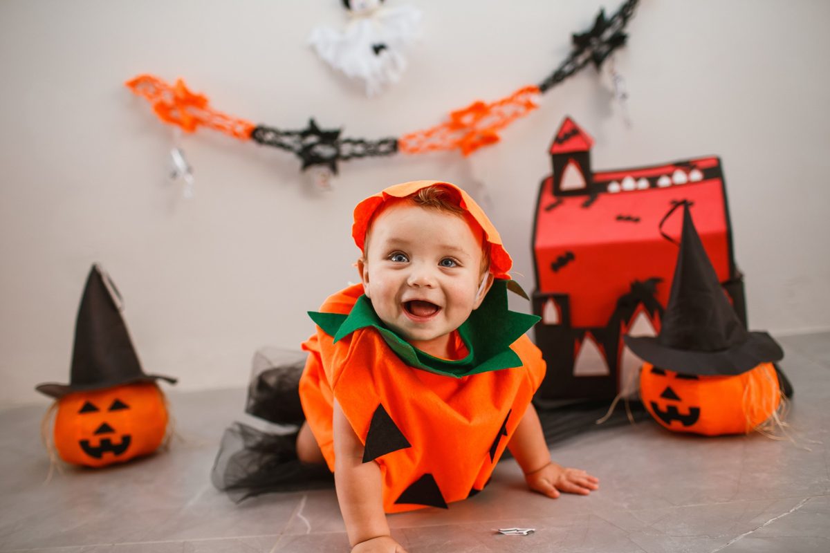 Bebé gateando con disfraz de calabaza de fieltro naranja, cuello de hojas verdes y tutú negro