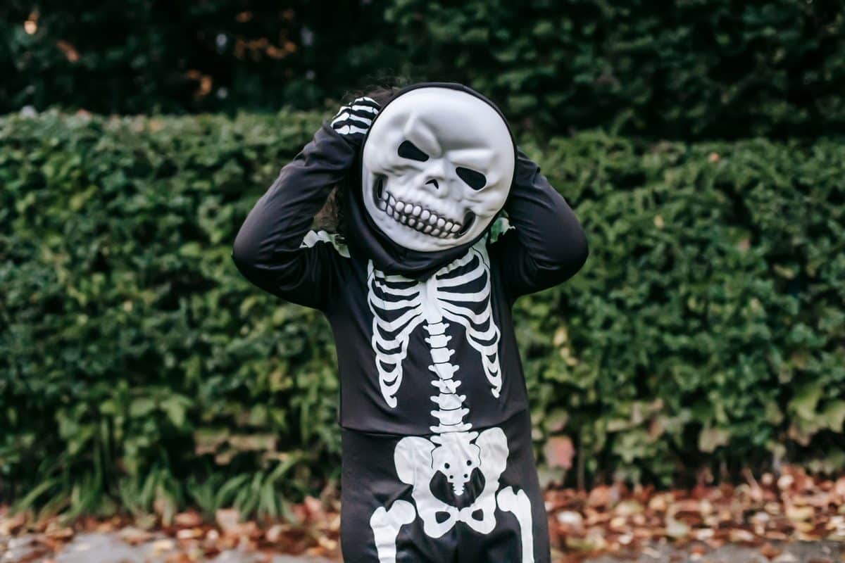 Niño con mono de esqueleto negro con huesos blancos y máscara de calavera, delante de un seto