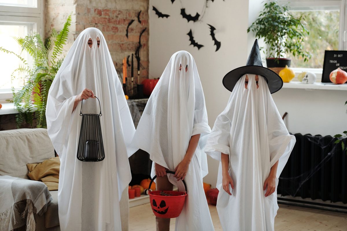 Tres niños disfrazados de fantasma con sábanas blancas, uno con sombrero de bruja y cesta de calabaza