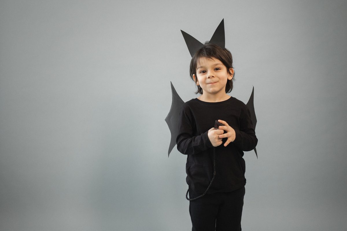 Niño vestido de negro con orejas y alas de murciélago de cartulina y cola de cordón trenzado
