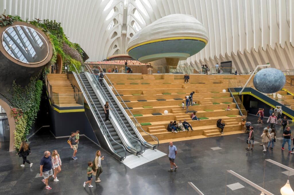 Familias y niños en la grada de madera de CaixaForum València, junto a las escaleras mecánicas y el Bosque vertical