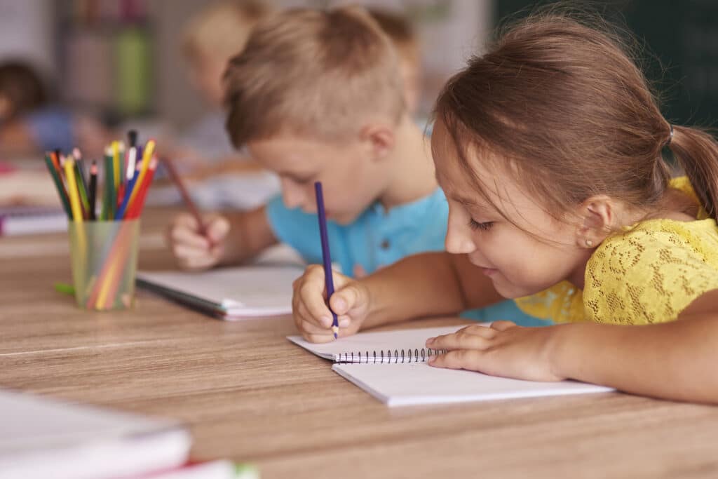 Niña y niño de Infantil dibujando en sus cuadernos con lápices de colores en una mesa del aula